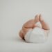 Cute baby lying on back in a diaper against a soft, white background.