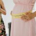 Close-up of a pregnant woman measuring her belly, symbolizing pregnancy health.